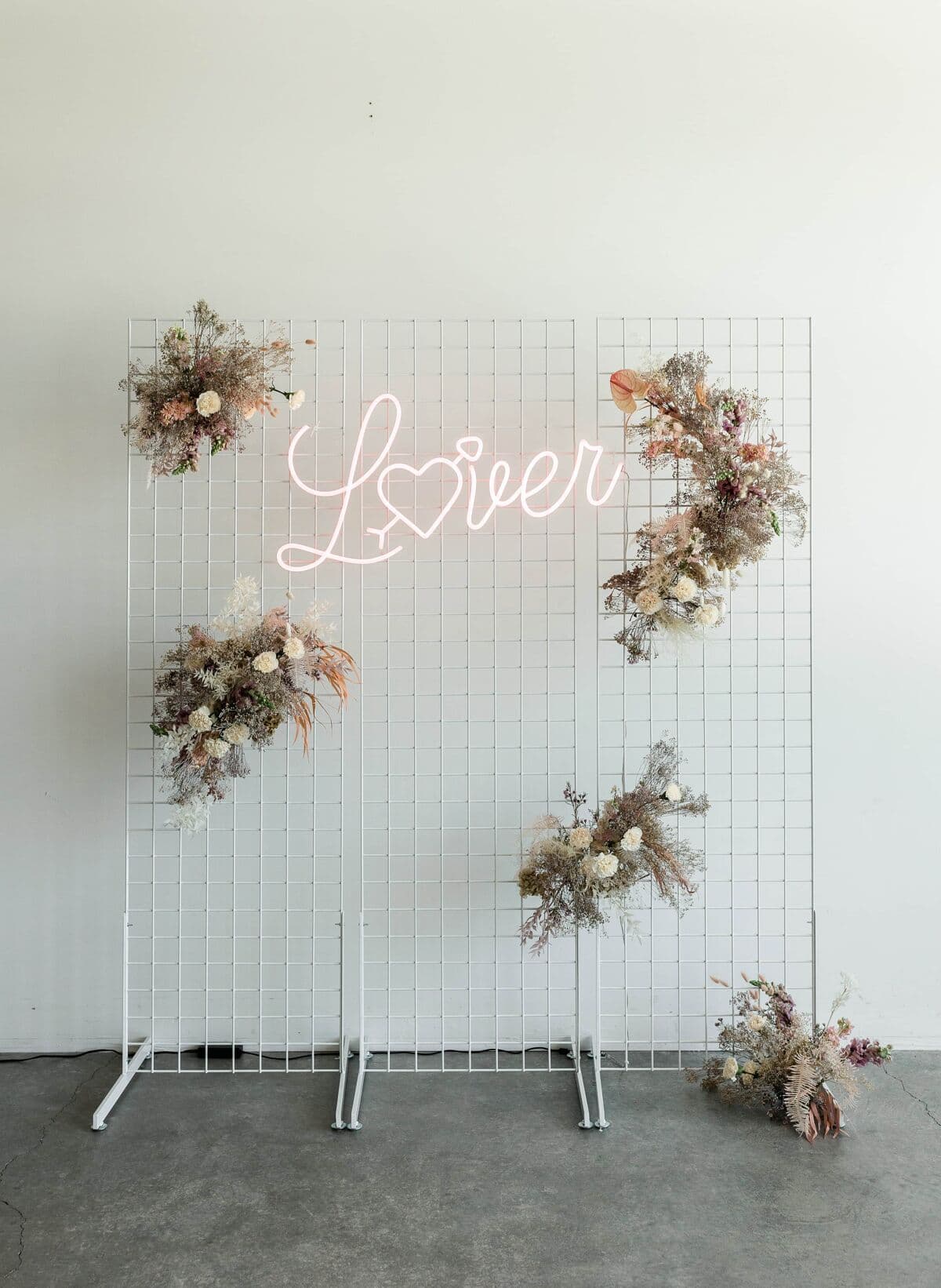Neon script sign mounted on a white grid wall dressed with dried florals